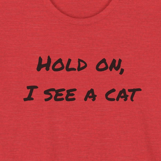 A heather red short-sleeve t-shirt with the black text 'HOLD ON, I SEE A CAT' printed across the chest, displayed on a solid white background.