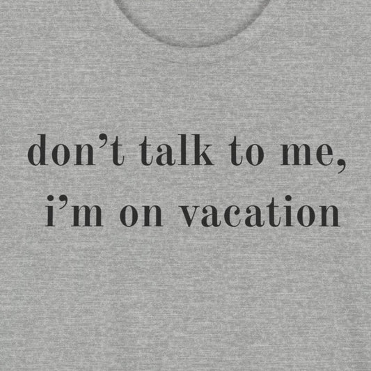 A heather gray short-sleeve t-shirt with the text 'don't talk to me, i'm on vacation' printed in black lowercase serif font across the chest, displayed on a solid white background.