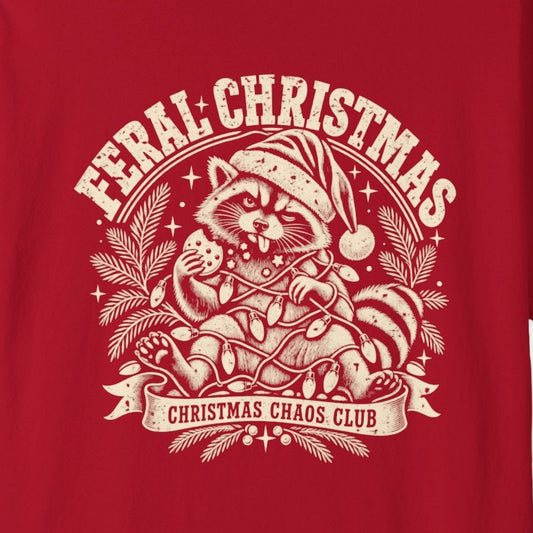 A red short-sleeve crewneck t-shirt featuring a cream-colored graphic print on the front with the text 'Feral Christmas' and an illustration of a raccoon in a Santa hat.