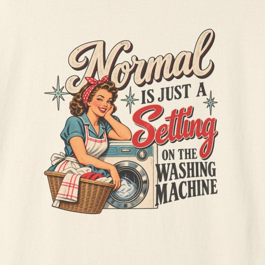 A cream-colored short-sleeve t-shirt with a vintage-style graphic of a pin-up woman washing a shirt next to a basket of laundry. The graphic text reads, 'Normal WASHING MACHINE IS JUST A Setting ON THE WASHING MACHINE'.