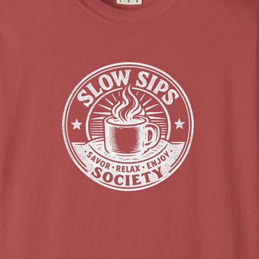 A dusty red short-sleeve crewneck t-shirt with a white circular graphic on the chest that reads 'SLOW SIPS SOCIETY' around an illustration of a coffee cup.