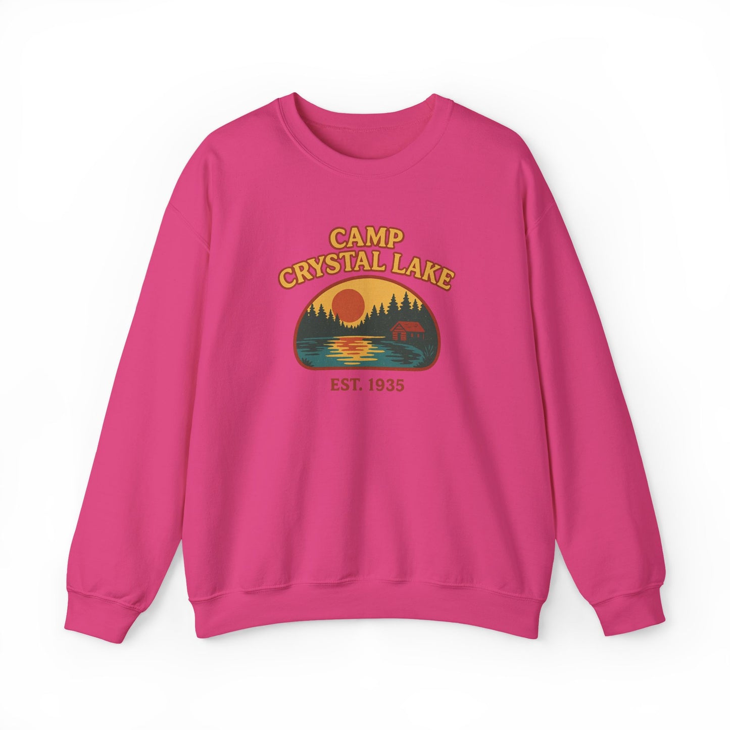 A bright pink crewneck sweatshirt featuring a retro-style 'Camp Crystal Lake' graphic on the chest with a sunset, pine trees, and a deer silhouette.