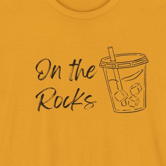 A mustard yellow short-sleeve t-shirt with a black graphic print on the front that reads 'On the Rocks' next to a simple line drawing of a bubble tea cup, shown against a plain white background.