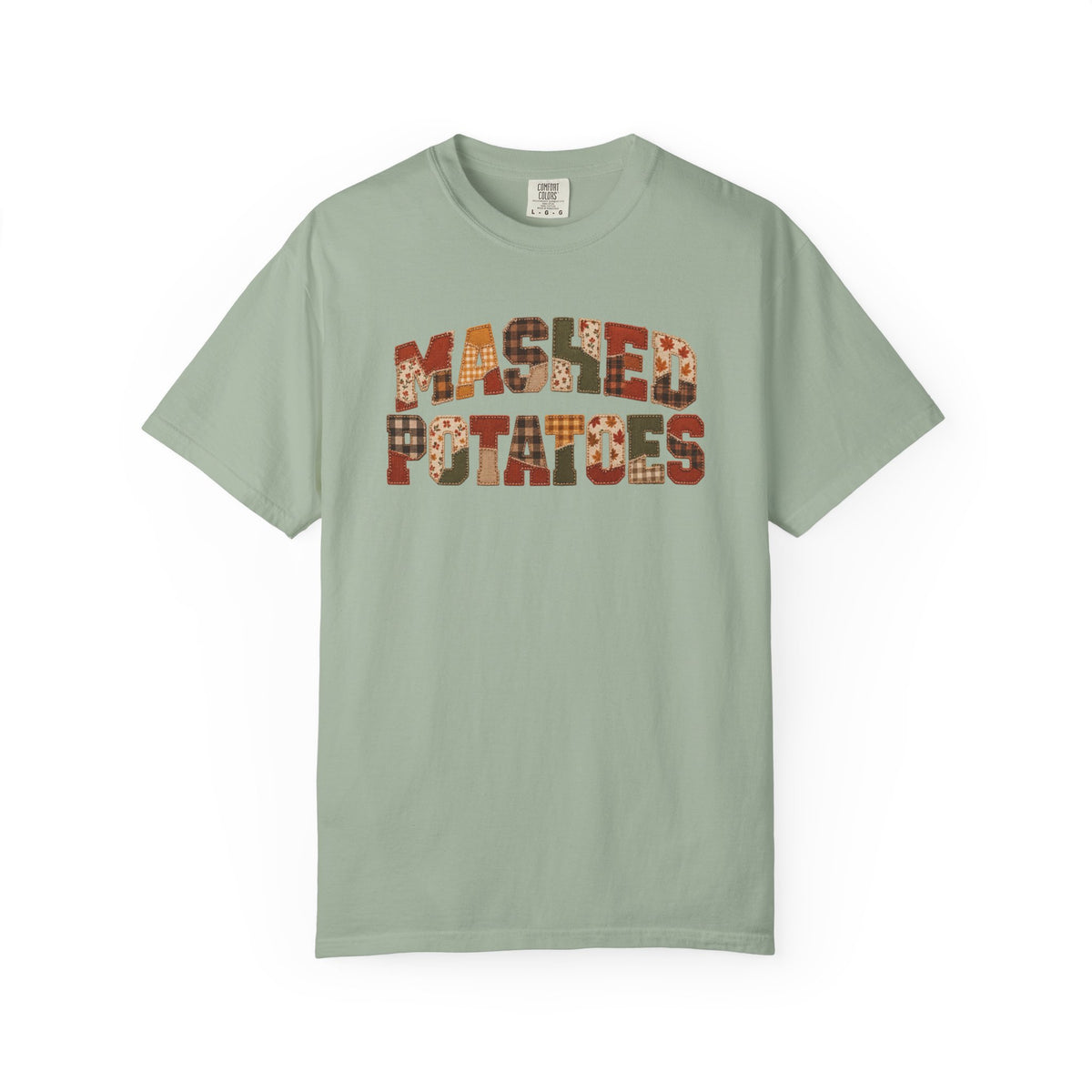 A sage green crewneck t-shirt featuring the words 'MASHED POTATOES' printed across the chest in a retro, patterned font with orange, brown, and white details, displayed on a clean white background.