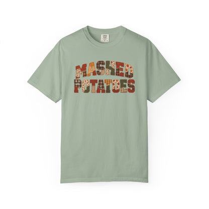 A sage green crewneck t-shirt featuring the words 'MASHED POTATOES' printed across the chest in a retro, patterned font with orange, brown, and white details, displayed on a clean white background.