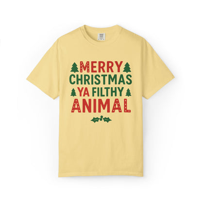 A pale yellow short-sleeve t-shirt with a festive graphic on the chest that reads 'MERRY CHRISTMAS YA FILTHY ANIMAL' in red and green lettering, accented with small green pine trees and holly leaves, shown on a plain white background.