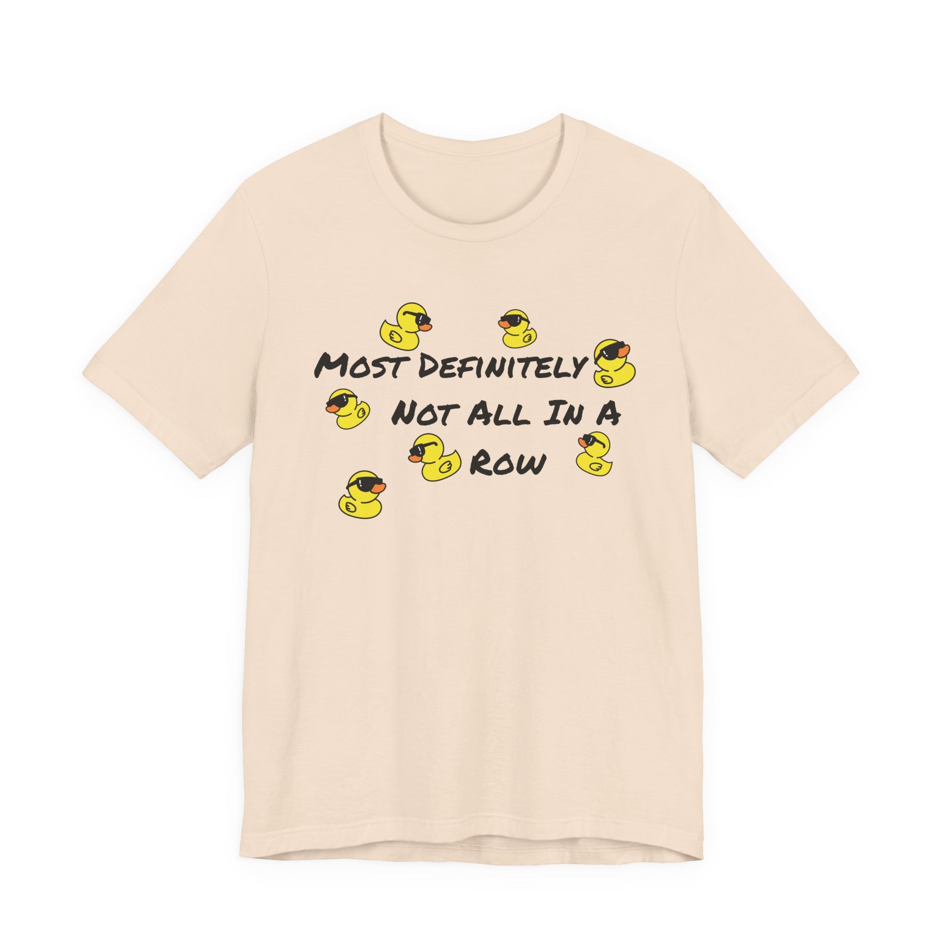 A light beige crewneck t-shirt featuring a graphic print of yellow rubber ducks and the text 'MOST DEFINITELY NOT ALL IN A ROW' in black.