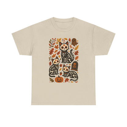 A light beige crewneck t-shirt featuring a central graphic print of four black cats decorated with sugar skull patterns, surrounded by orange and brown autumn leaves, pumpkins, and tombstones.