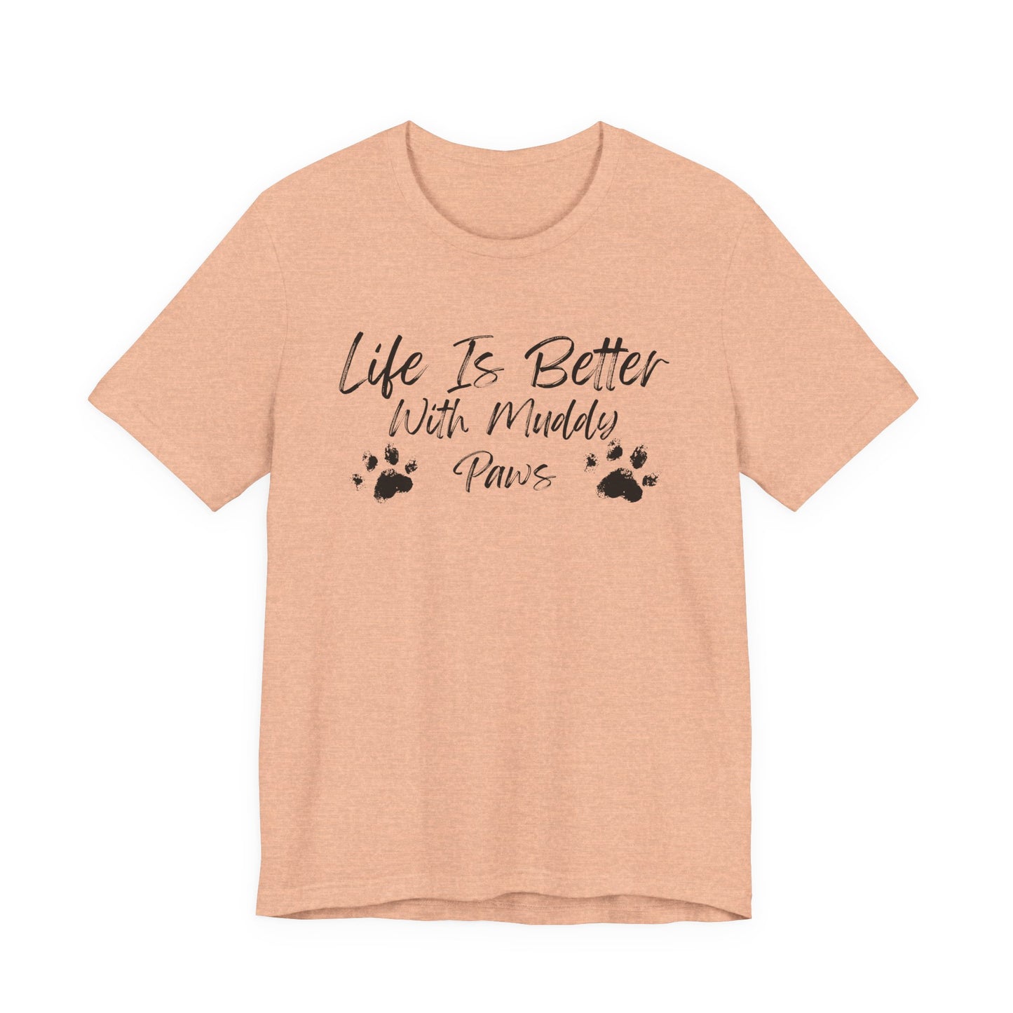 A heather peach short-sleeve t-shirt with a black graphic print that reads 'Life Is Better With Muddy Paws' accompanied by two paw prints, shown on a plain white background.