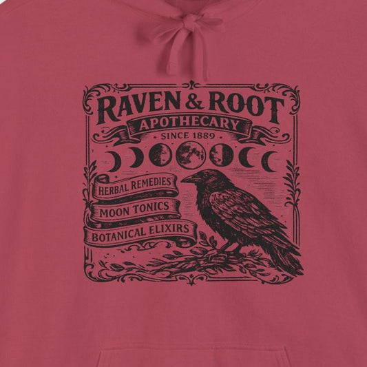 A dusty rose pink pullover hoodie with a black graphic print on the chest featuring a raven and the text 'RAVEN & ROOT'.