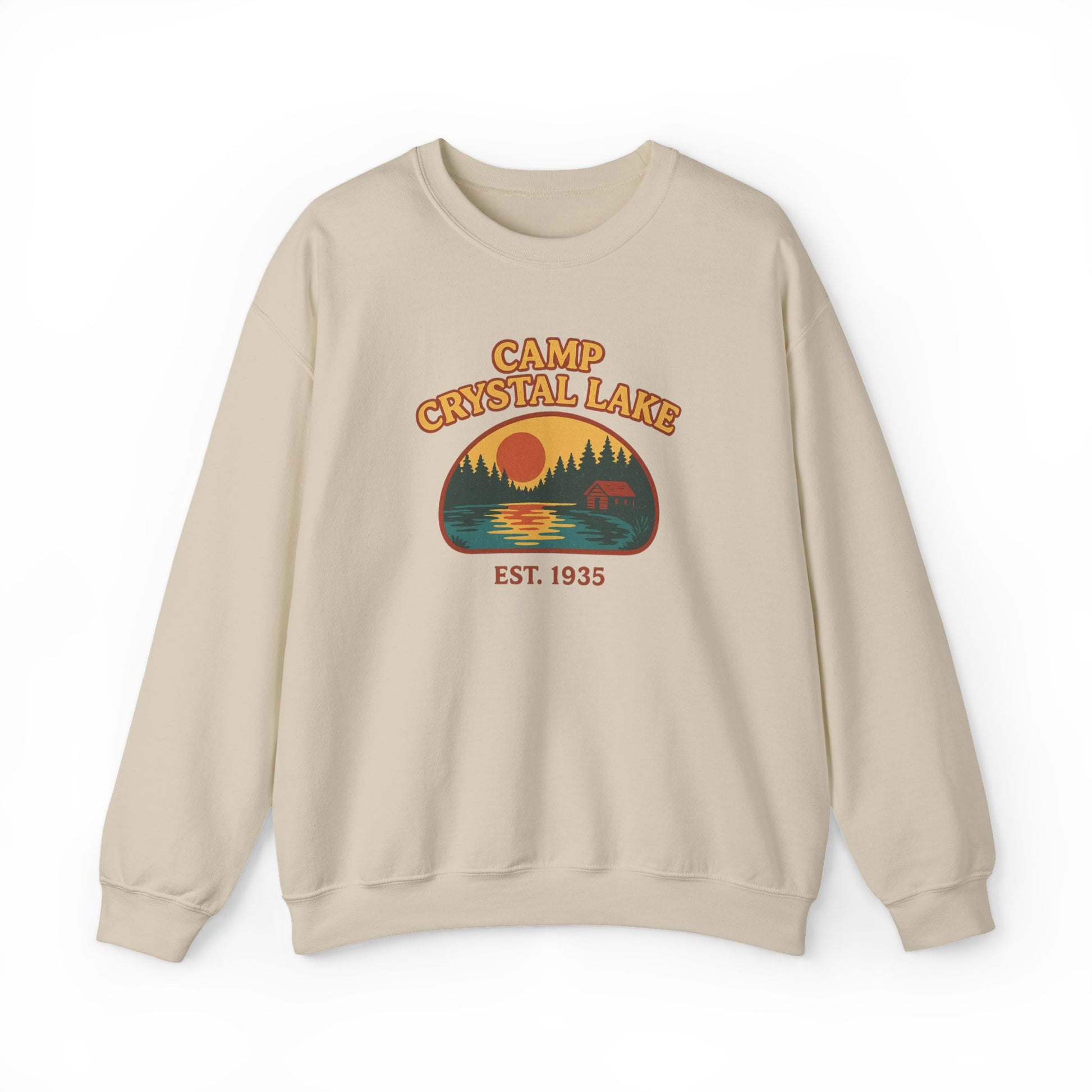 A beige crewneck sweatshirt featuring a retro-style graphic of a campfire scene at Crystal Lake with the text 'CAMP CRYSTAL LAKE' and 'EST. 1935'.