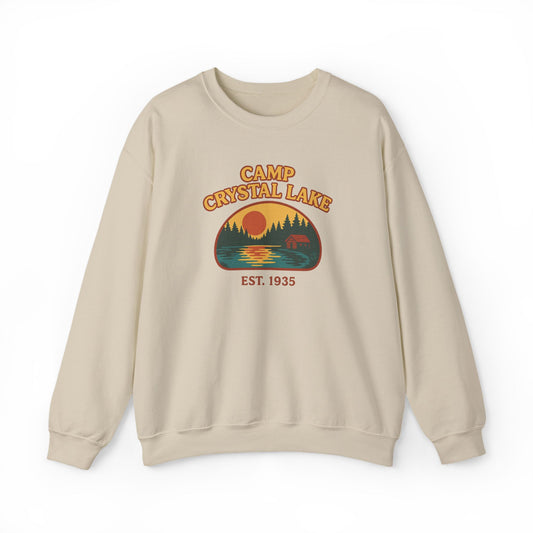 A beige crewneck sweatshirt featuring a retro-style graphic of a campfire scene at Crystal Lake with the text 'CAMP CRYSTAL LAKE' and 'EST. 1935'.