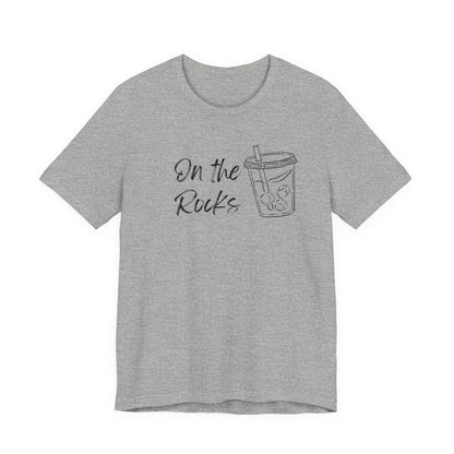 A heather gray short-sleeve t-shirt with a black graphic print on the front that reads 'On the Rocks' next to a simple line drawing of a iced coffee cup, shown against a plain white background.