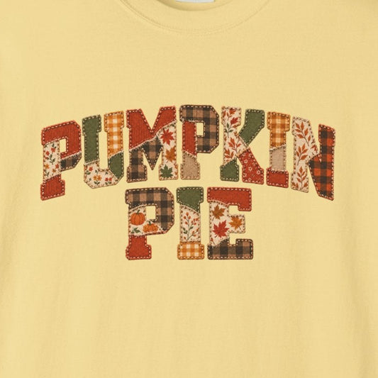 A pale yellow short-sleeve t-shirt with a graphic reading 'PUMPKIN PIE' in a decorative autumn-themed patterned font, displayed on a clean white background.