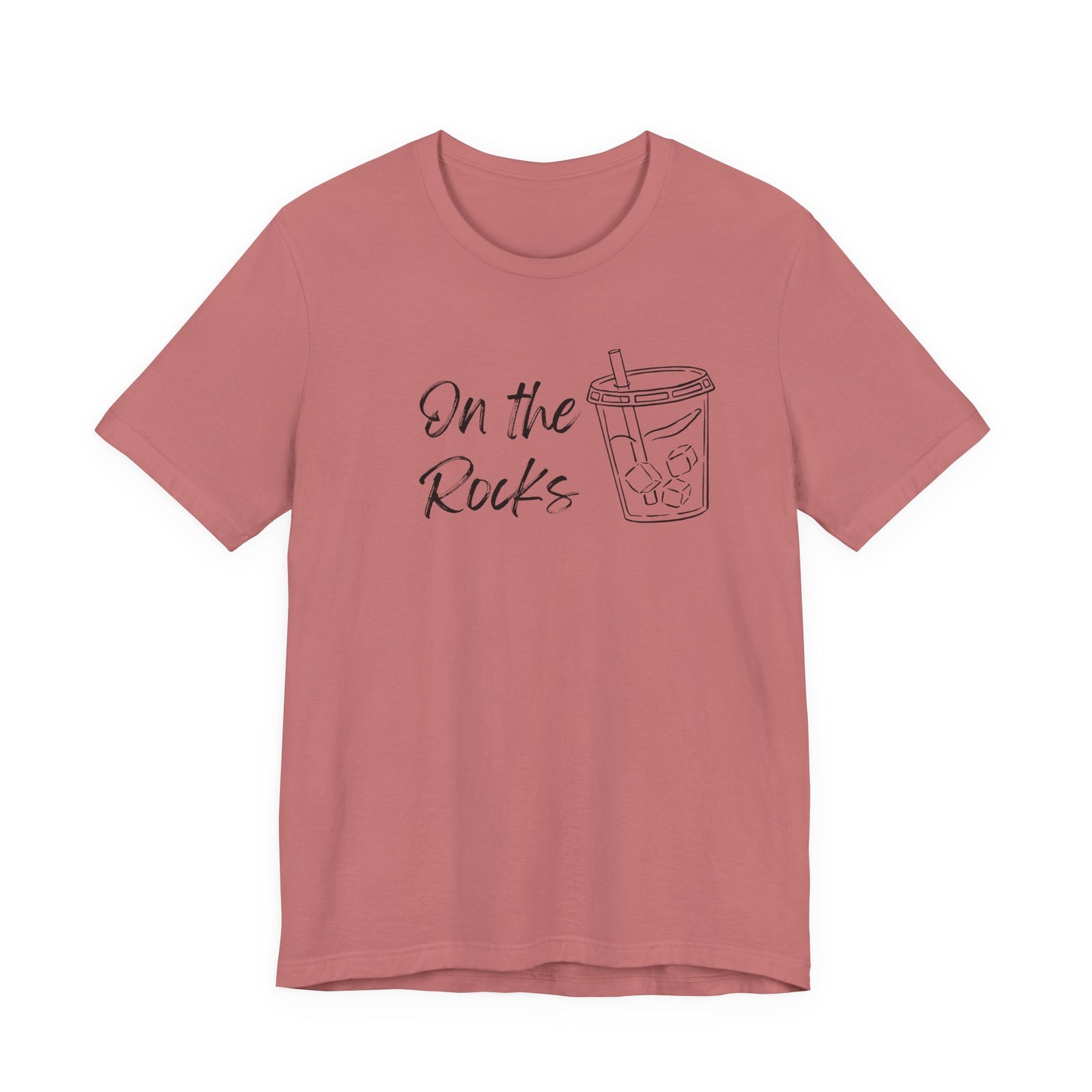 A dusty rose short-sleeve t-shirt with a black graphic print on the front that reads 'On the Rocks' next to a simple line drawing of a iced coffee cup, shown against a plain white background.