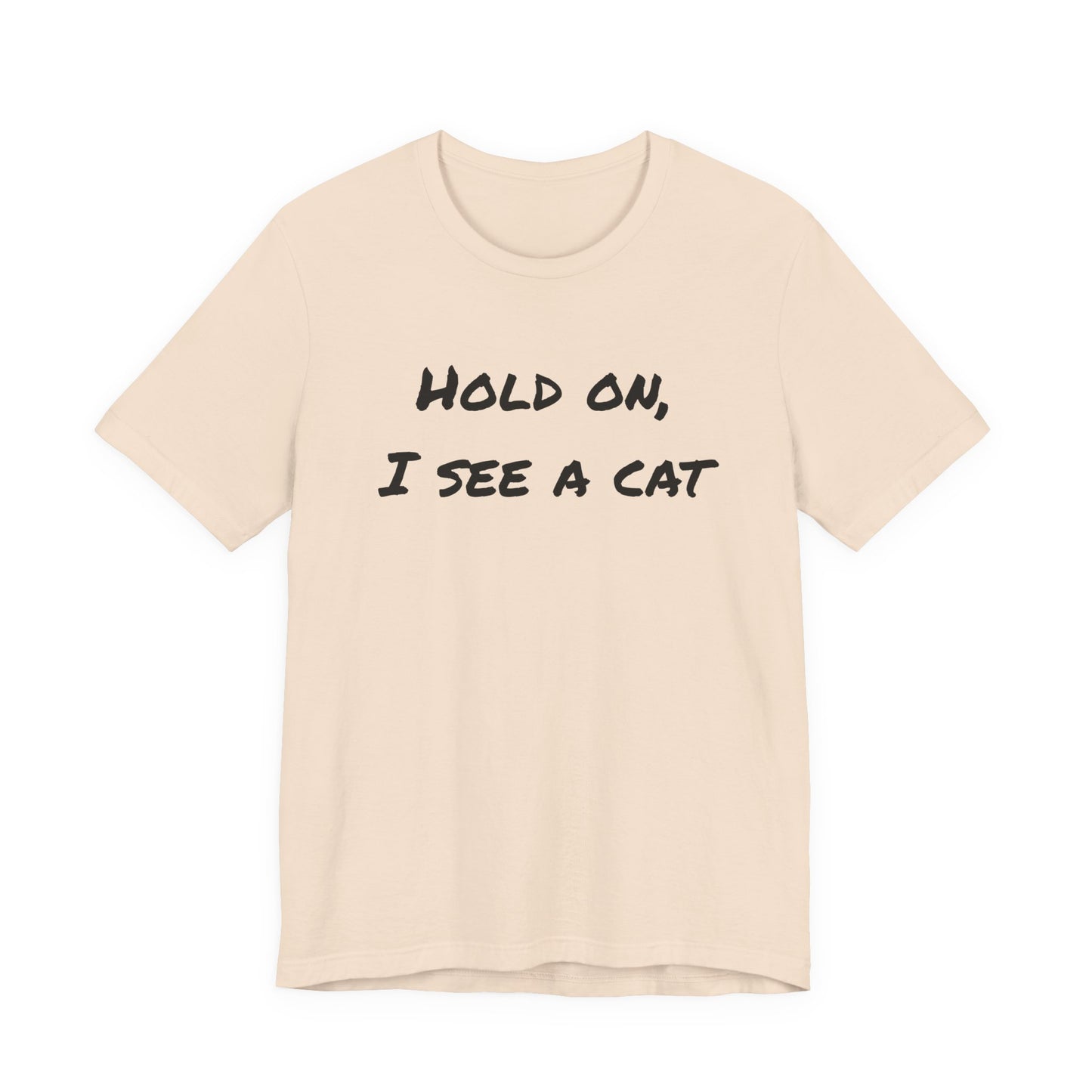 A light beige crewneck t-shirt with the phrase 'HOLD ON, I SEE A CAT' printed in a black handwritten-style font across the chest, displayed on a solid white background.