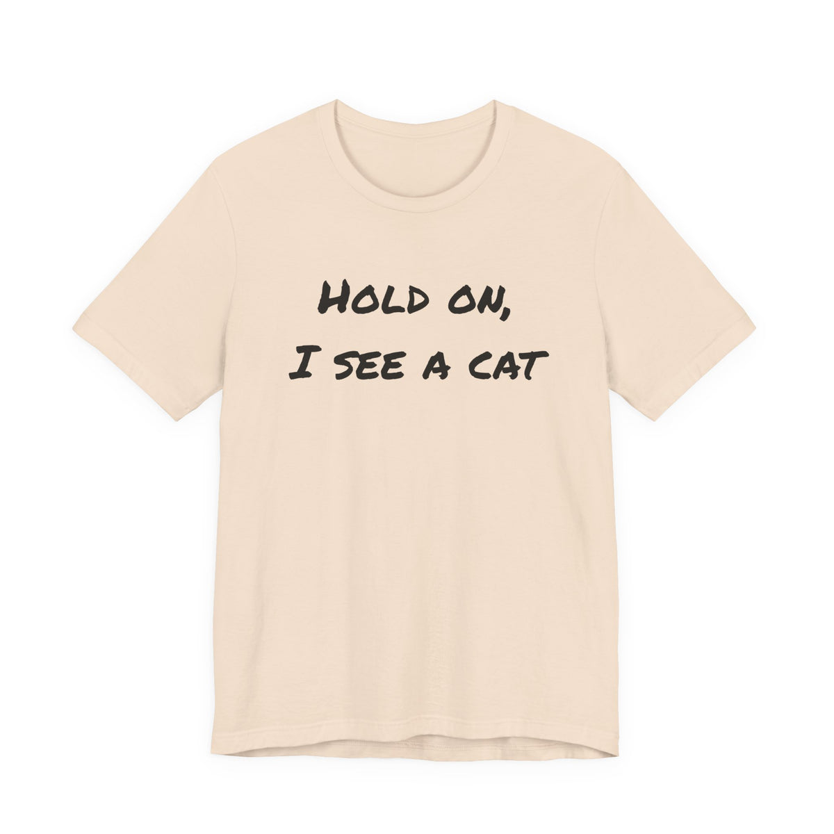 A light beige crewneck t-shirt with the phrase 'HOLD ON, I SEE A CAT' printed in a black handwritten-style font across the chest, displayed on a solid white background.