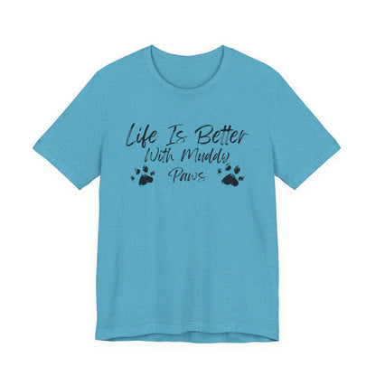 A light blue short-sleeve crewneck t-shirt with a black graphic print on the front that reads 'Life Is Better With Muddy Paws' accompanied by two black paw prints, shown against a plain white background.