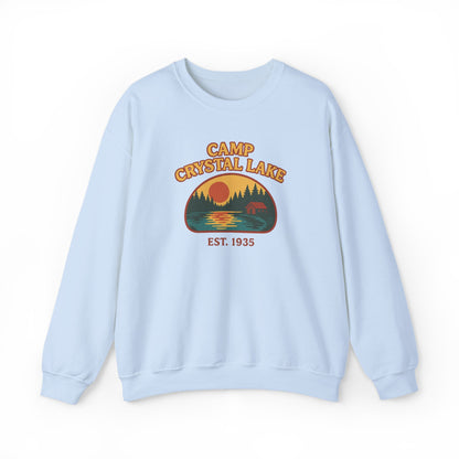 A light blue crewneck sweatshirt featuring a retro-style graphic of a bear at Crystal Lake with the text 'CAMP CRYSTAL LAKE' and 'EST. 1935' on the front, displayed against a plain white background.