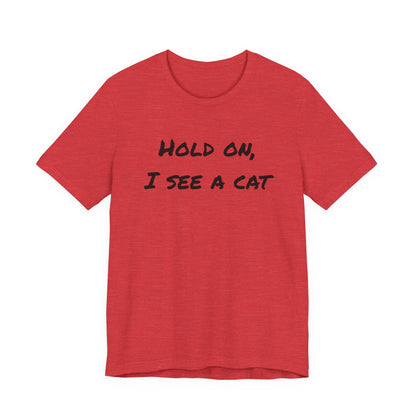A heather red short-sleeve t-shirt with the black text 'HOLD ON, I SEE A CAT' printed across the chest, displayed on a solid white background.