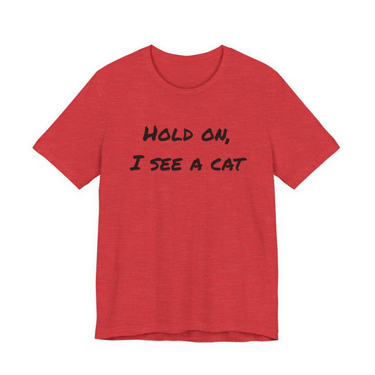 A heather red short-sleeve t-shirt with the black text 'HOLD ON, I SEE A CAT' printed across the chest, displayed on a solid white background.