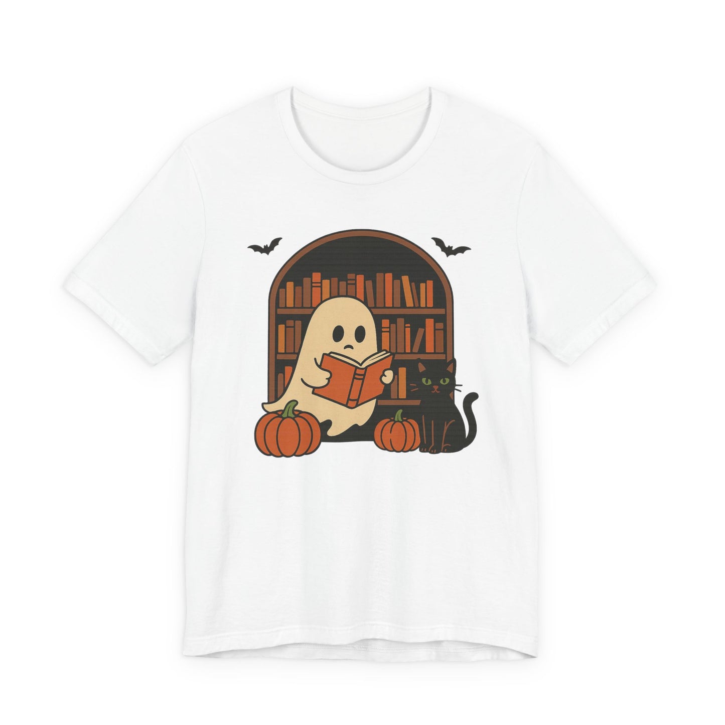 A white short-sleeve crewneck t-shirt featuring a cute Halloween graphic of a ghost reading a book in front of a bookshelf, with pumpkins, a black cat, and bats.