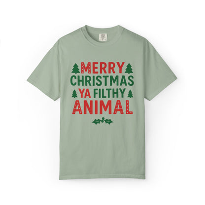 A sage green short-sleeve t-shirt with a festive Christmas graphic that reads 'MERRY CHRISTMAS YA FILTHY ANIMAL' in red and green lettering, accented with small pine tree icons, shown on a plain white background.