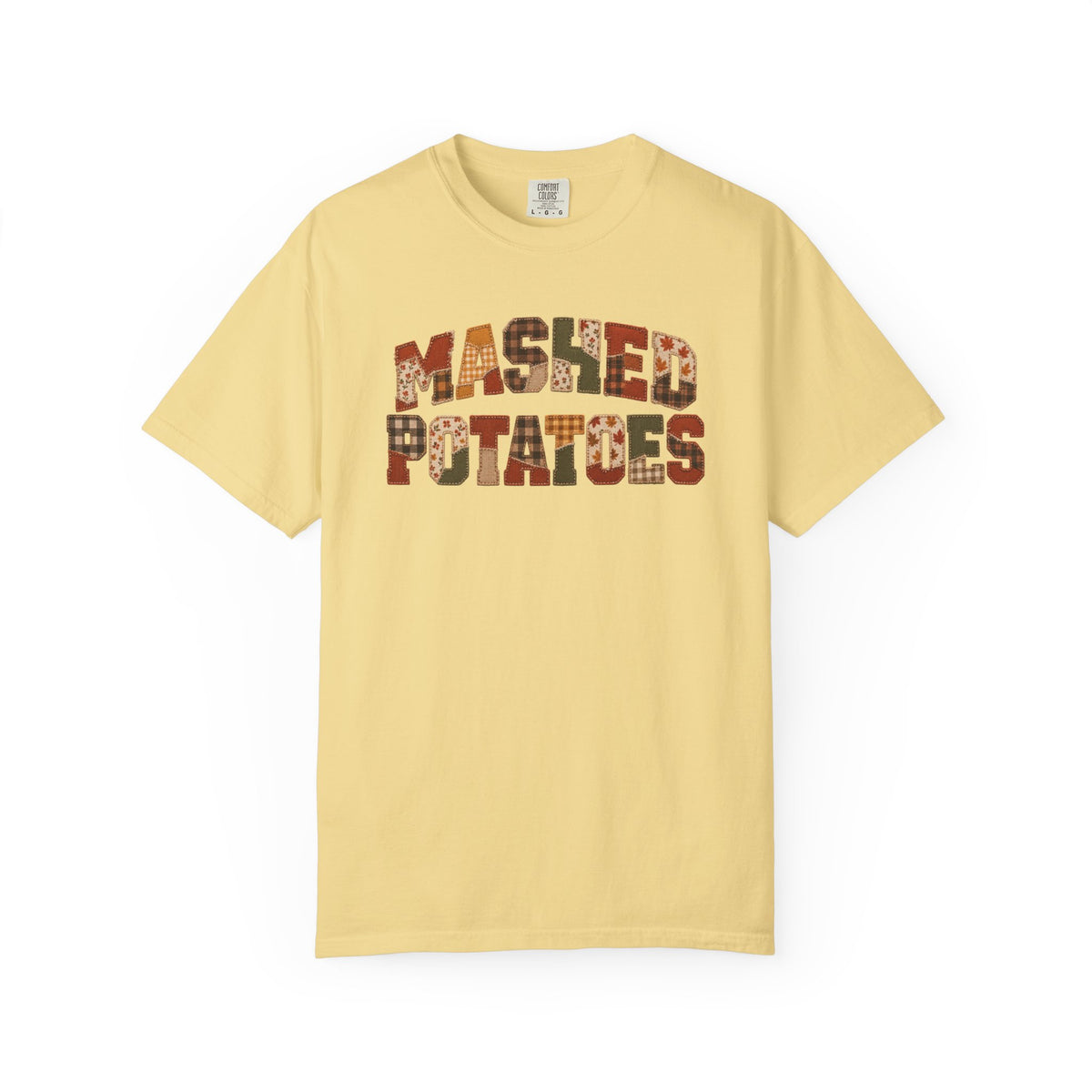 A pale yellow short-sleeve t-shirt with 'MASHED POTATOES' printed across the chest in a rustic brown and beige patterned font, displayed on a clean white background.