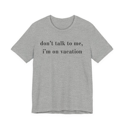 A heather gray short-sleeve t-shirt with the text 'don't talk to me, i'm on vacation' printed in black lowercase serif font across the chest, displayed on a solid white background.