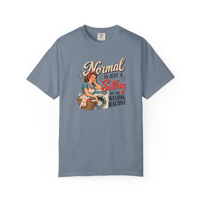 A slate blue short-sleeve t-shirt with a vintage-style graphic of a pin-up woman washing a shirt, accompanied by the text 'Normal is just a Setting for the Washing Machine'.