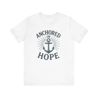 A white short-sleeve crewneck t-shirt featuring a dark gray graphic print on the front with the words 'ANCHORED IN HOPE' surrounding an anchor and sunburst design.
