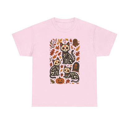 A light pink short-sleeve crewneck t-shirt featuring a central graphic print of three black cats decorated with sugar skull patterns, surrounded by autumn leaves, pumpkins, and a tombstone.