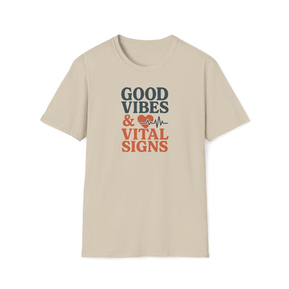 A beige short-sleeve crewneck t-shirt with a graphic on the chest that reads 'GOOD VIBES & VITAL SIGNS' in dark gray and orange lettering, accompanied by a small red heart and heartbeat line icon, shown on a plain white background.