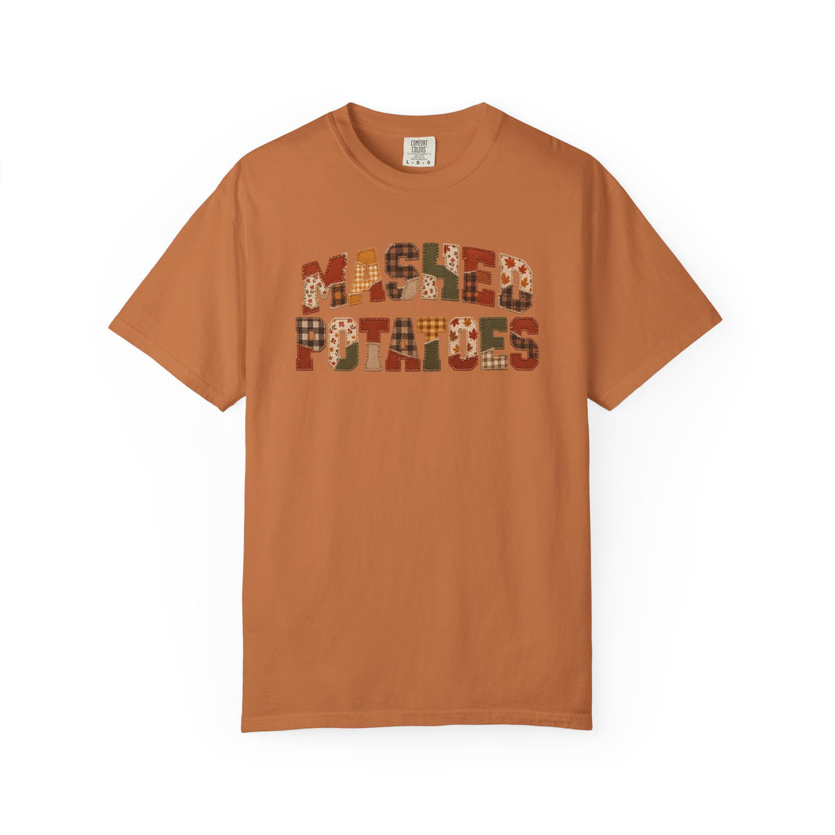 A rust-orange short-sleeve t-shirt with 'Mashed Potatoes' printed across the chest in a patchwork pattern of autumnal colors, shown against a plain white background.
