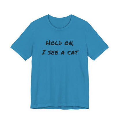 A bright blue short-sleeve crewneck t-shirt with the text 'HOLD ON, I SEE A CAT' printed in black across the chest, displayed on a solid white background.