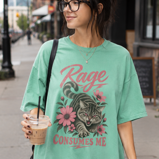 A woman wearing an oversized mint green graphic t-shirt with a cat illustration and the text 'Rage Consumes Me', holding an iced coffee on a city sidewalk.