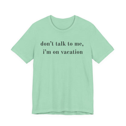 A mint green short-sleeve t-shirt with the text 'don't talk to me, i'm on vacation' printed in black serif font across the chest, displayed on a solid white background.