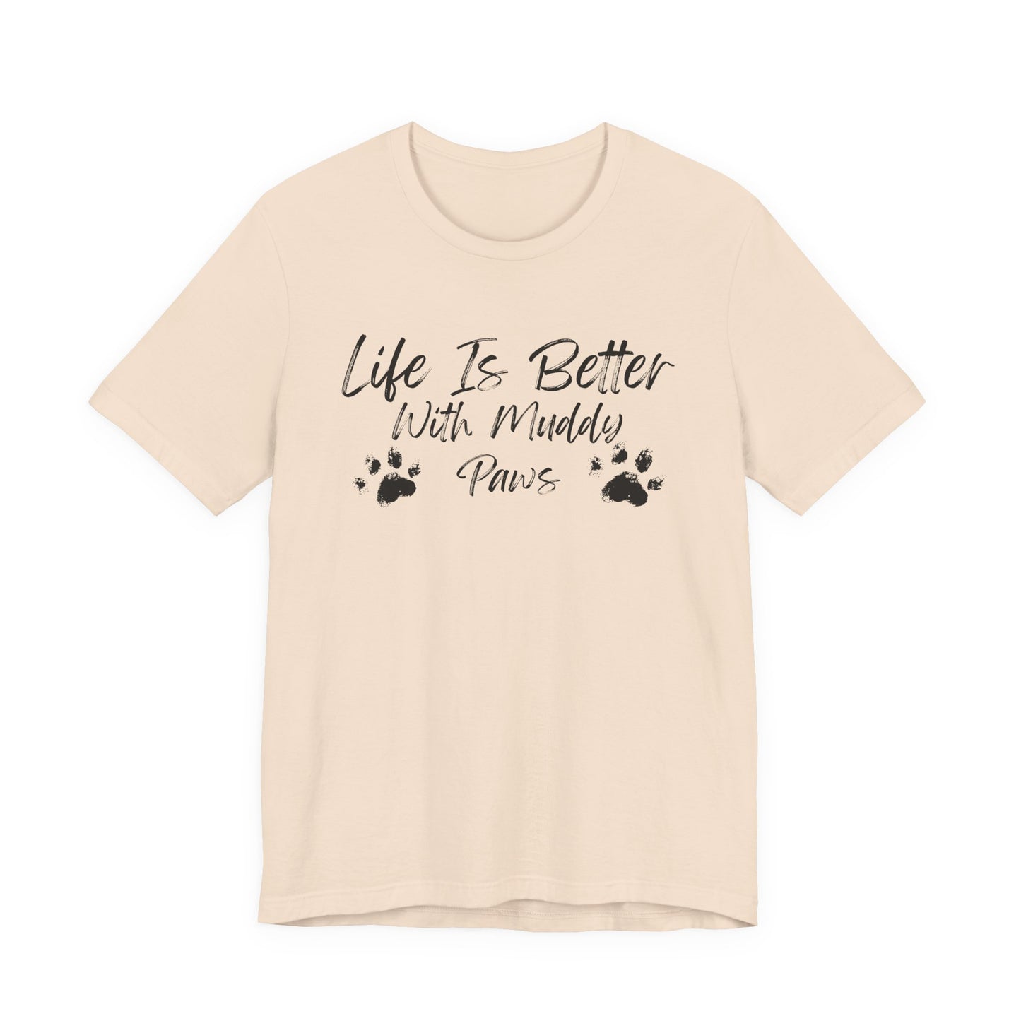 A light beige short-sleeve t-shirt with a black graphic print on the front that reads 'Life Is Better With Muddy Paws' accompanied by two paw prints, shown against a plain white background.