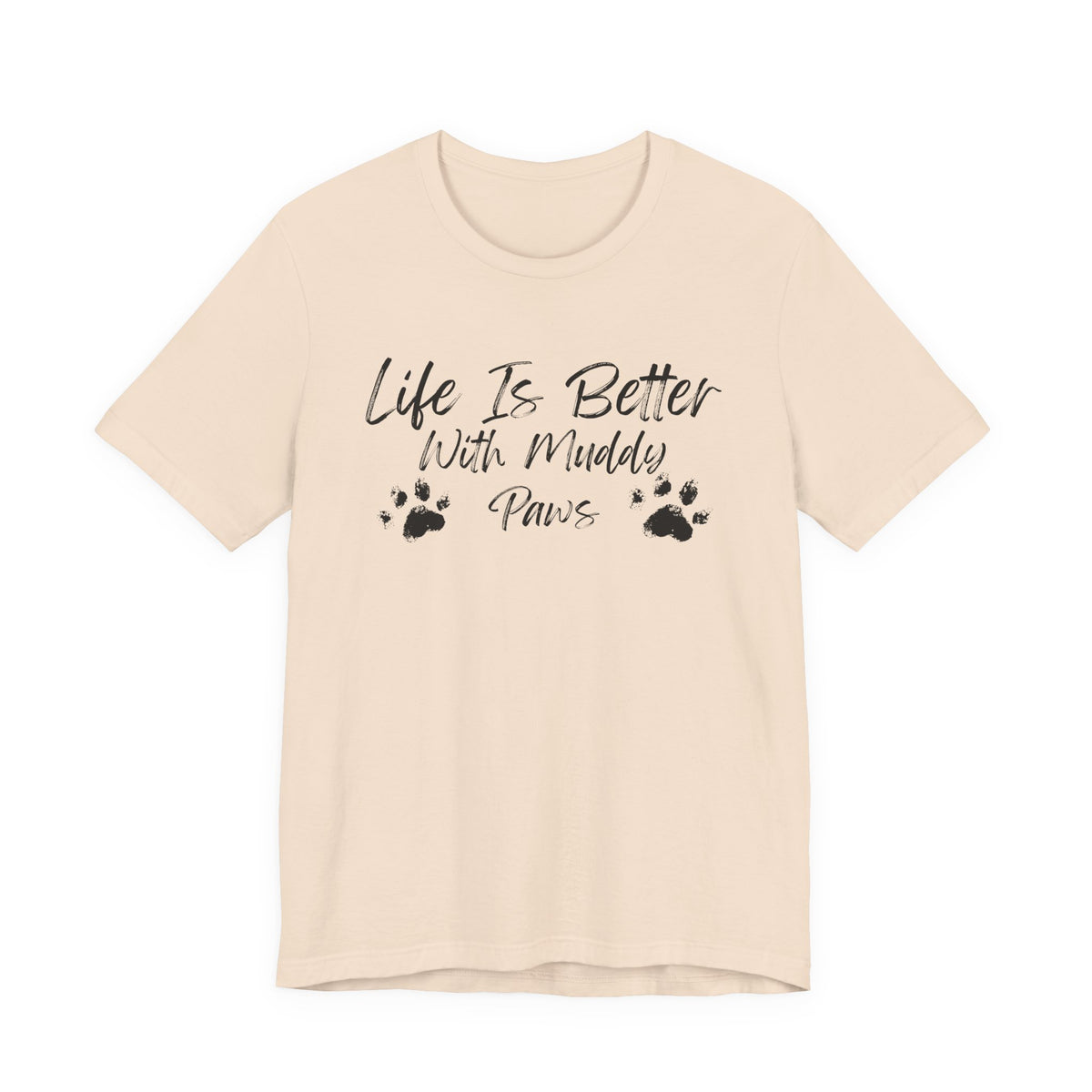 A light beige short-sleeve t-shirt with a black graphic print on the front that reads 'Life Is Better With Muddy Paws' accompanied by two paw prints, shown against a plain white background.