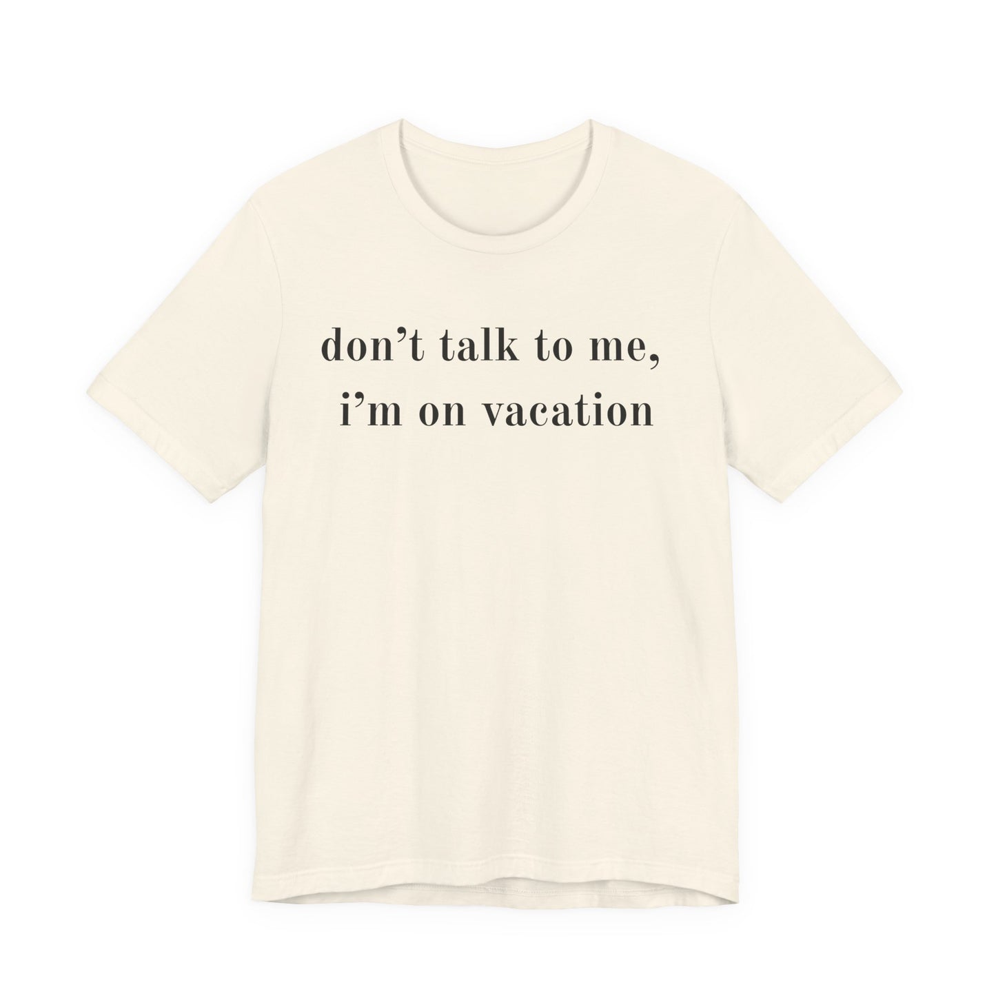 An off-white short-sleeve crewneck t-shirt with the text 'don't talk to me, i'm on vacation' printed in black serif font across the chest, displayed on a solid white background.