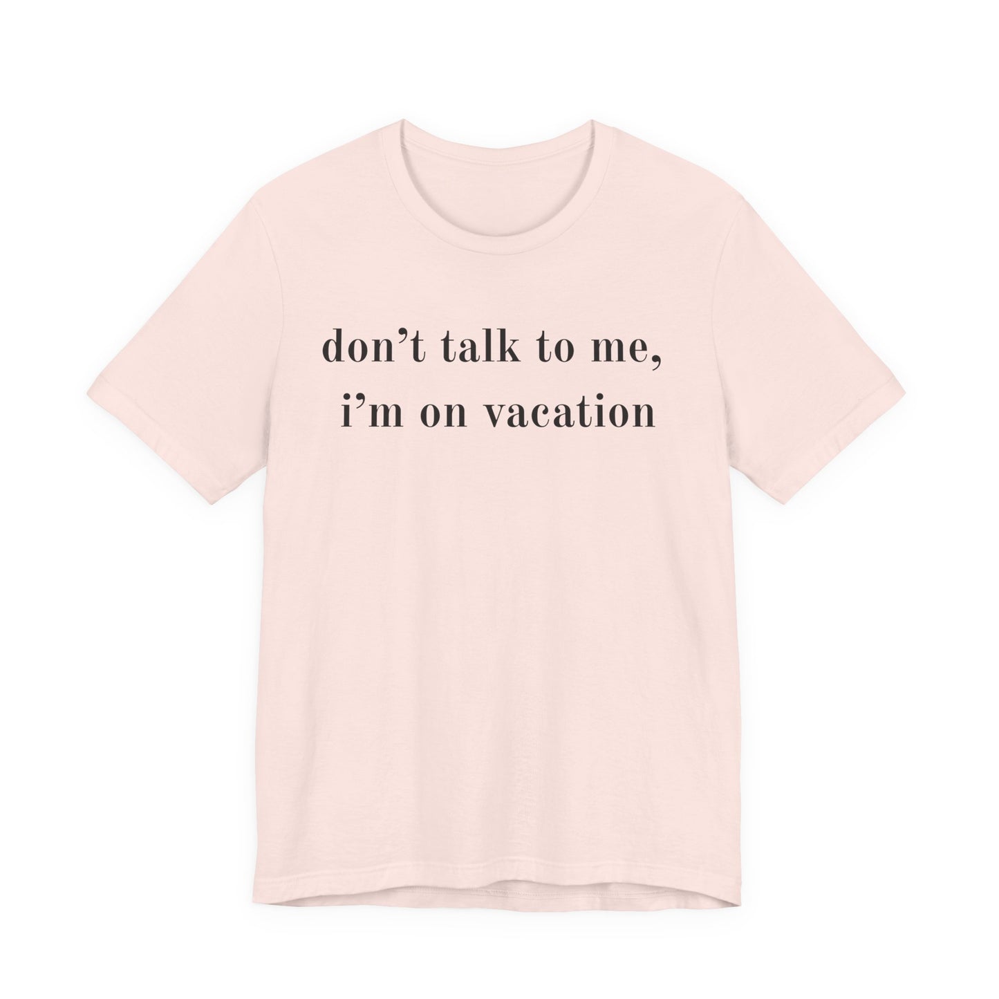 A light pink short-sleeve crewneck t-shirt with the text 'don't talk to me, i'm on vacation' printed in black serif font across the chest, displayed on a solid white background.