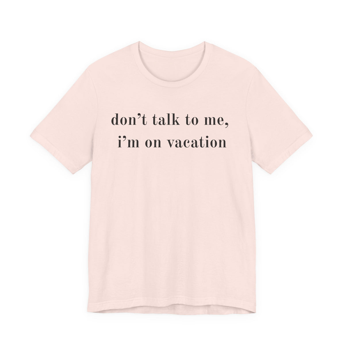 A light pink short-sleeve crewneck t-shirt with the text 'don't talk to me, i'm on vacation' printed in black serif font across the chest, displayed on a solid white background.