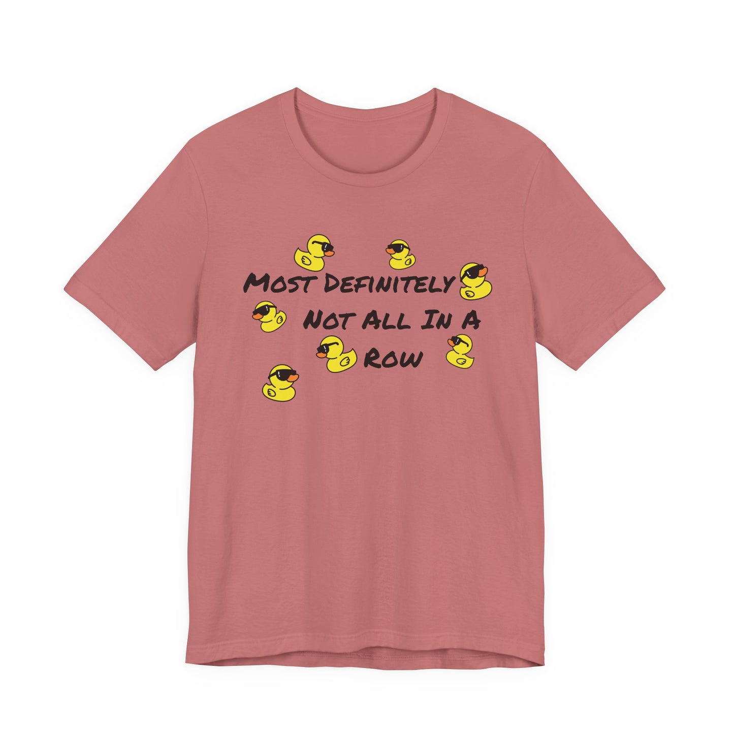 A dusty rose short-sleeve t-shirt with a graphic print on the front. The graphic features the text 'MOST DEFINITELY NOT ALL IN A ROW' in black, interspersed with small yellow rubber ducks wearing black sunglasses.