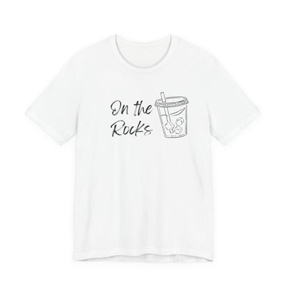A white short-sleeve crewneck t-shirt featuring a black graphic print on the front with the text 'On the Rocks' next to a simple line drawing of a iced coffee cup.