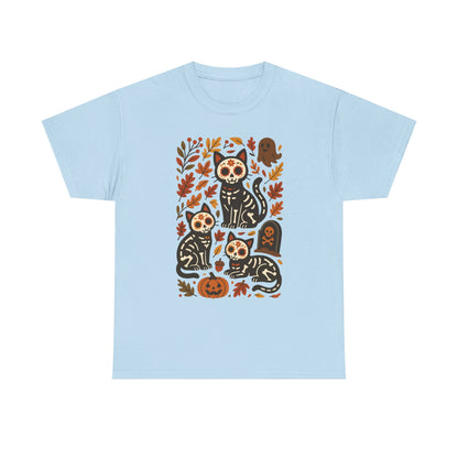 A light blue short-sleeve crewneck t-shirt featuring a central graphic print of four black cats with sugar skull makeup surrounded by autumn leaves, pumpkins, and tombstones.