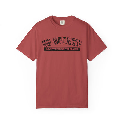 A dusty red short-sleeve t-shirt with a black graphic print on the chest reading 'GO SPORTS' and 'I'M JUST HERE FOR THE SNACKS'.