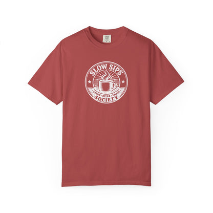 A dusty red short-sleeve crewneck t-shirt with a white circular graphic on the chest that reads 'SLOW SIPS SOCIETY' around an illustration of a coffee cup.
