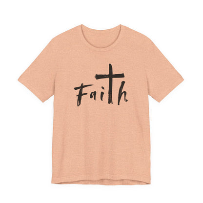 A heather peach short-sleeve t-shirt with a black graphic on the chest featuring a cross and the word 'Faith' in a handwritten font, displayed on a solid white background.