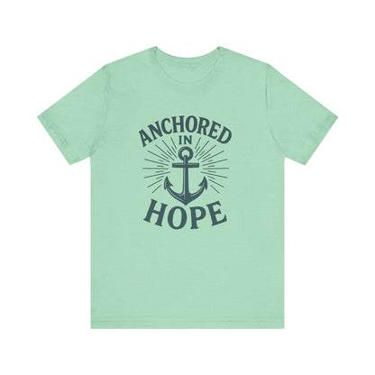 A mint green short-sleeve t-shirt with a dark navy graphic on the front featuring an anchor and the words 'ANCHORED IN HOPE'.