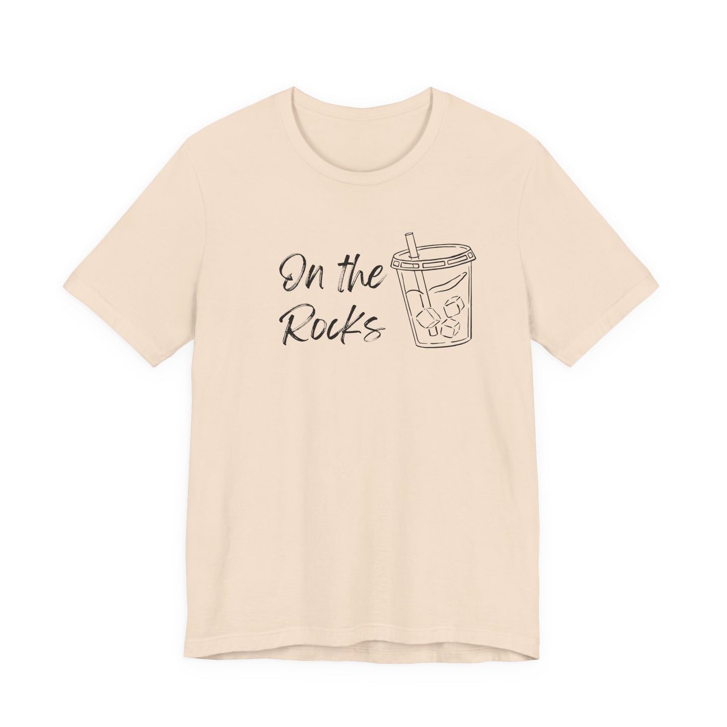 A light beige short-sleeve t-shirt with a black graphic print on the front that reads 'On the Rocks' next to a simple line drawing of a iced coffee cup, shown against a plain white background.